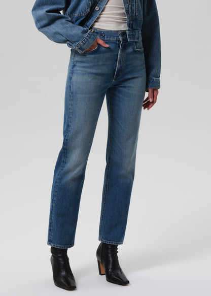 Person wearing a blue denim jacket and jeans on a grey background