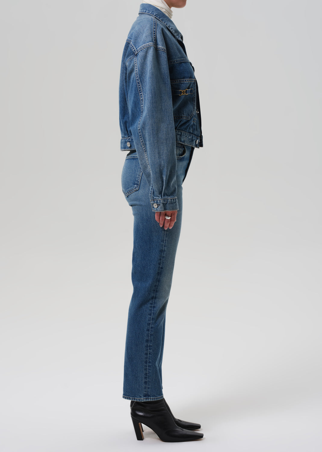 Person wearing a blue denim jacket and jeans on a grey background