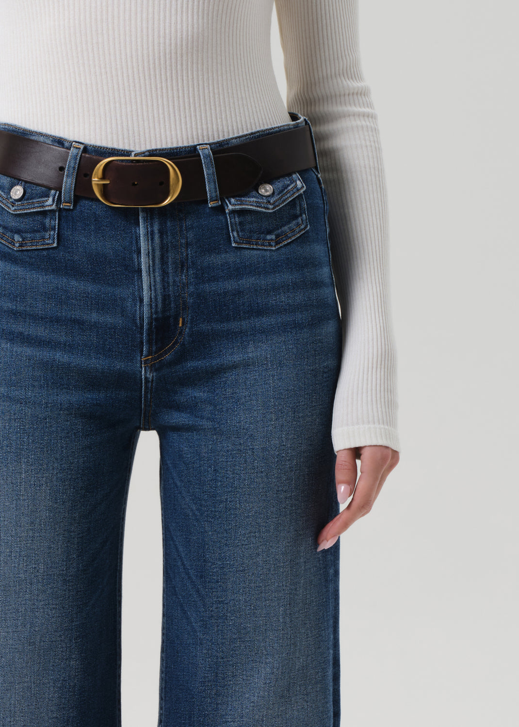 Person wearing blue jeans with a black belt on a plain background