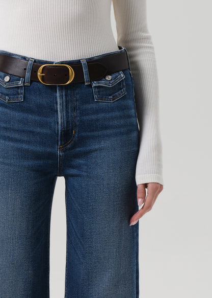 Person wearing blue jeans with a black belt on a plain background
