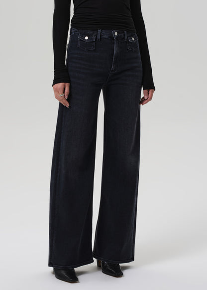 Person wearing black turtleneck and wide-leg jeans on a grey background