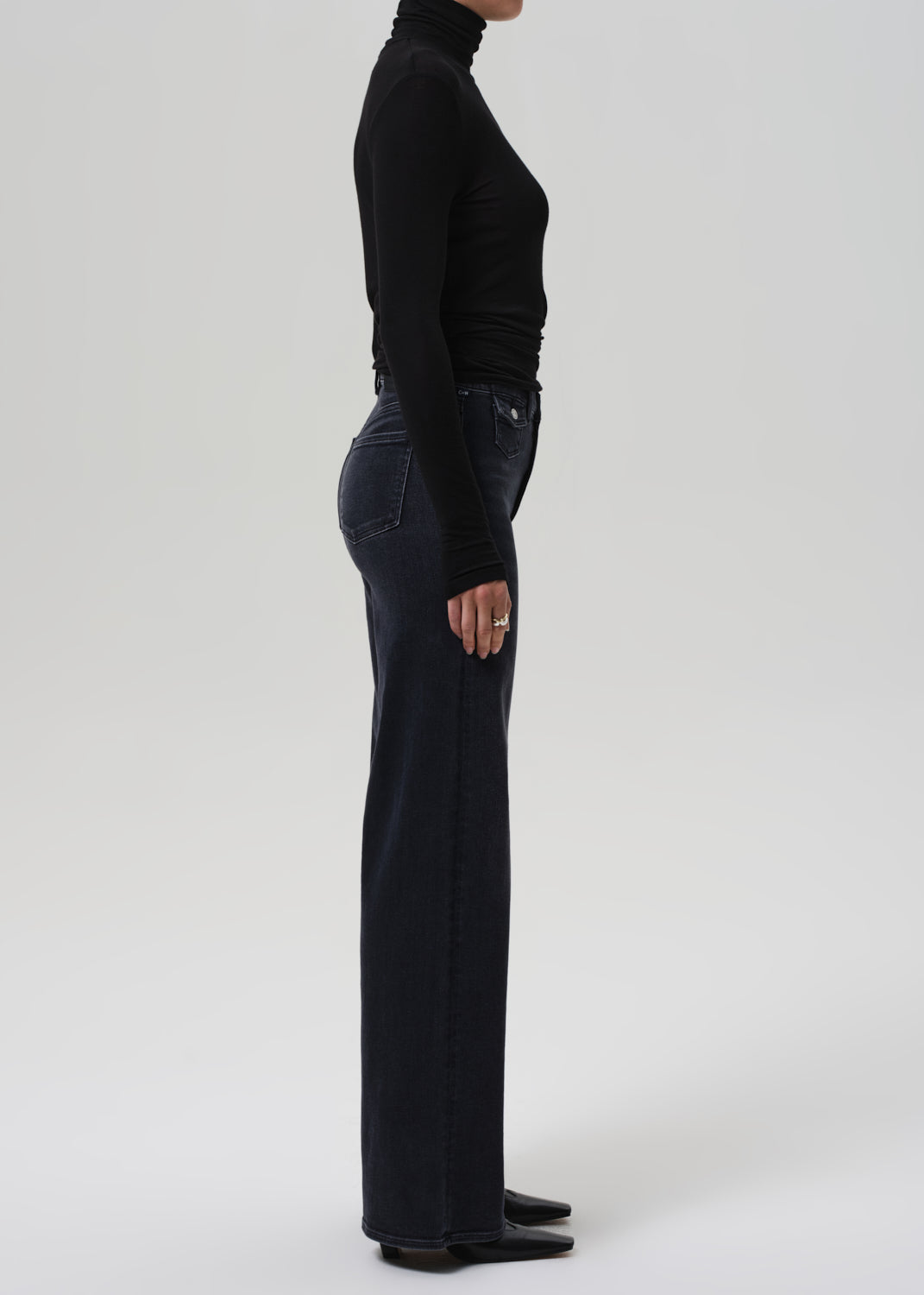 Person wearing black turtleneck and wide-leg jeans on a grey background