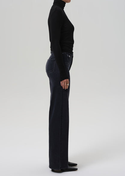 Person wearing black turtleneck and wide-leg jeans on a grey background