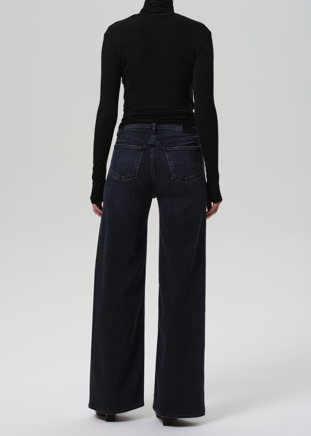 Person wearing black turtleneck and wide-leg jeans on a grey background