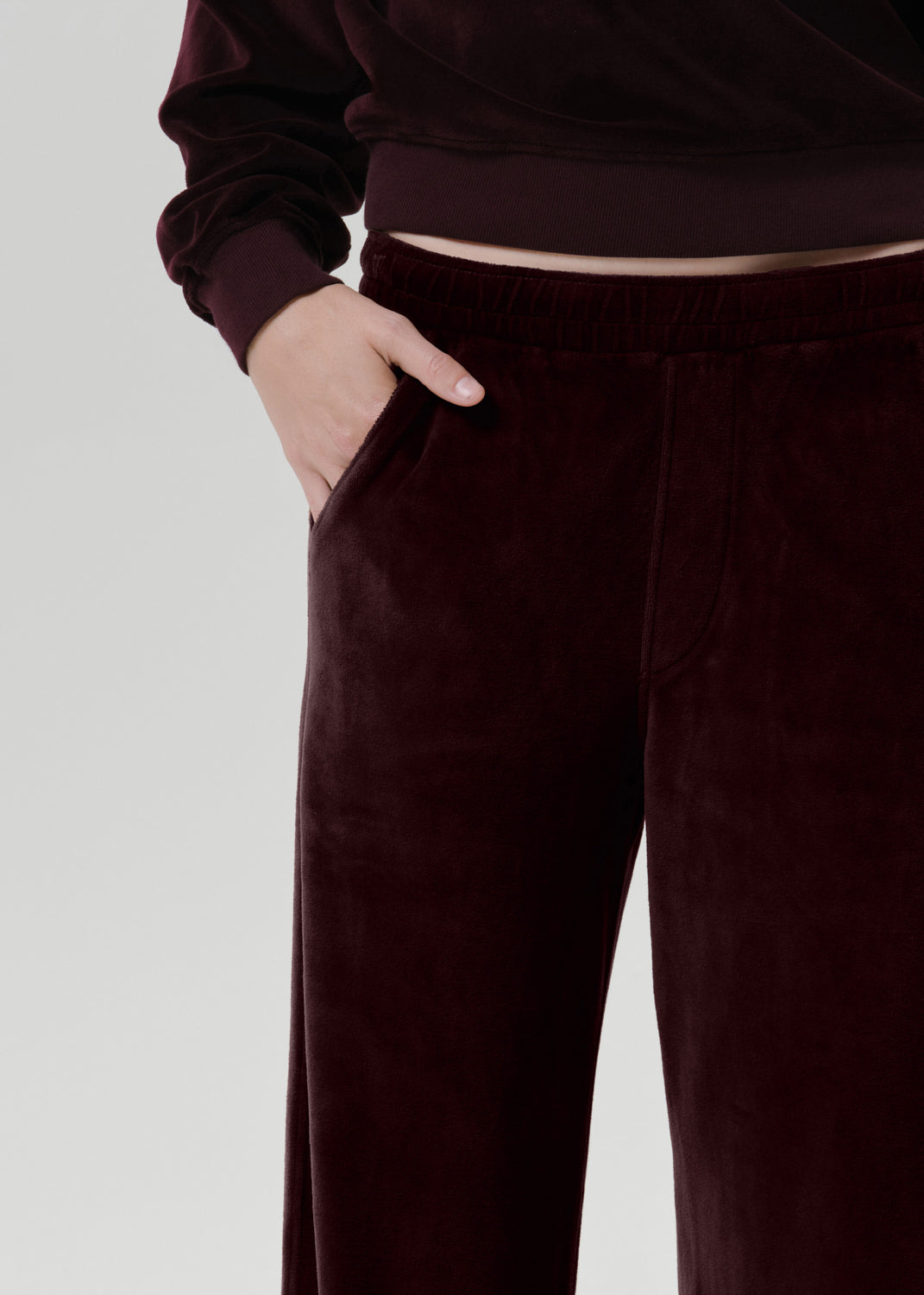 Close-up of a person wearing dark burgundy velvet wide-leg pants with a matching top, showing the side pocket and hand.