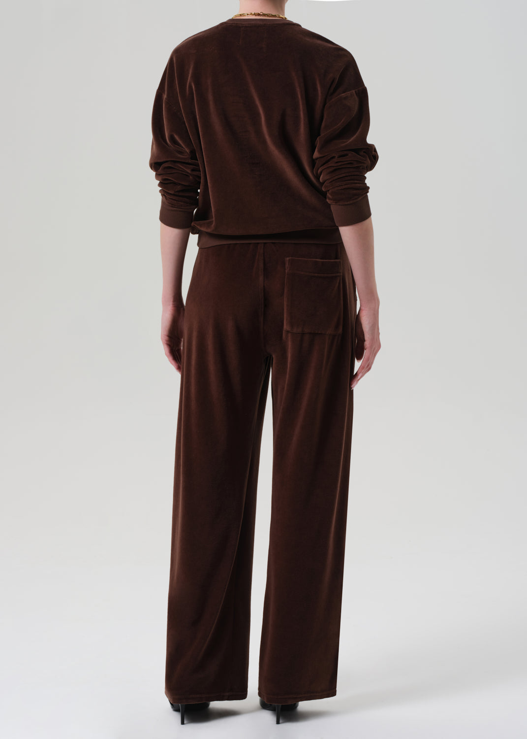 Person wearing a brown matching velour set on a grey background