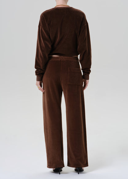 A model viewed from the back wearing a matching brown velvet long-sleeve crop top and wide-leg trousers set, paired with black pointed-toe heels against a grey background.