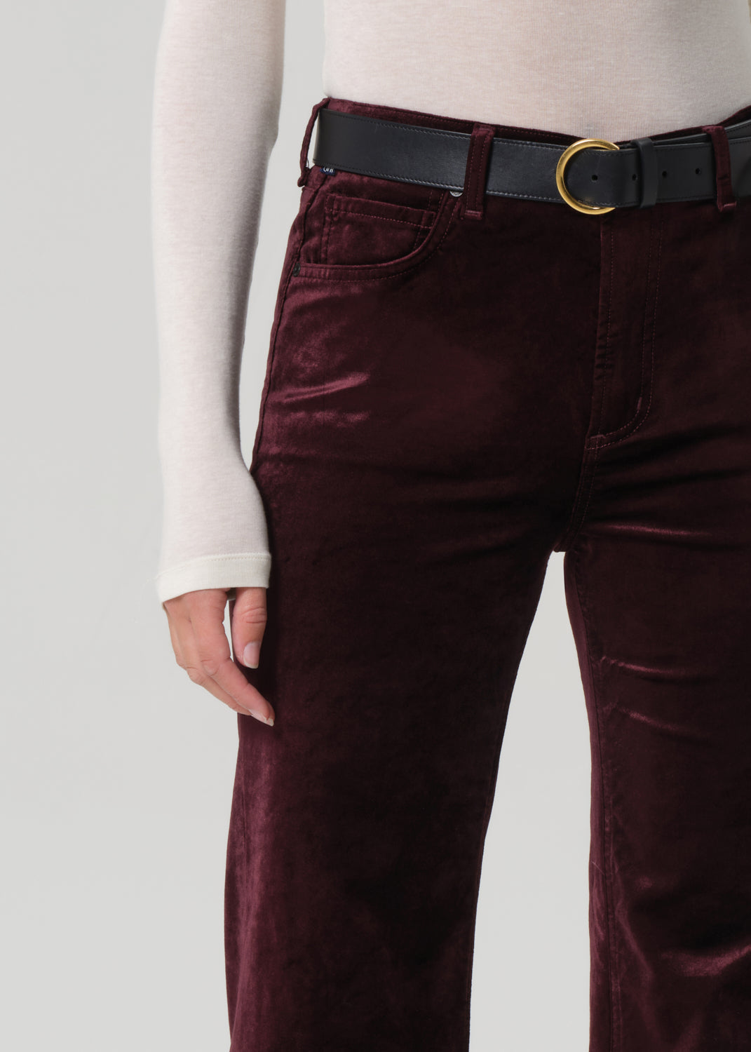 Burgundy velvet pants with a black belt on a plain background