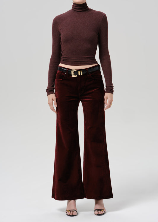 Person wearing a burgundy fitted turtleneck with burgundy wide leg pants on a grey background