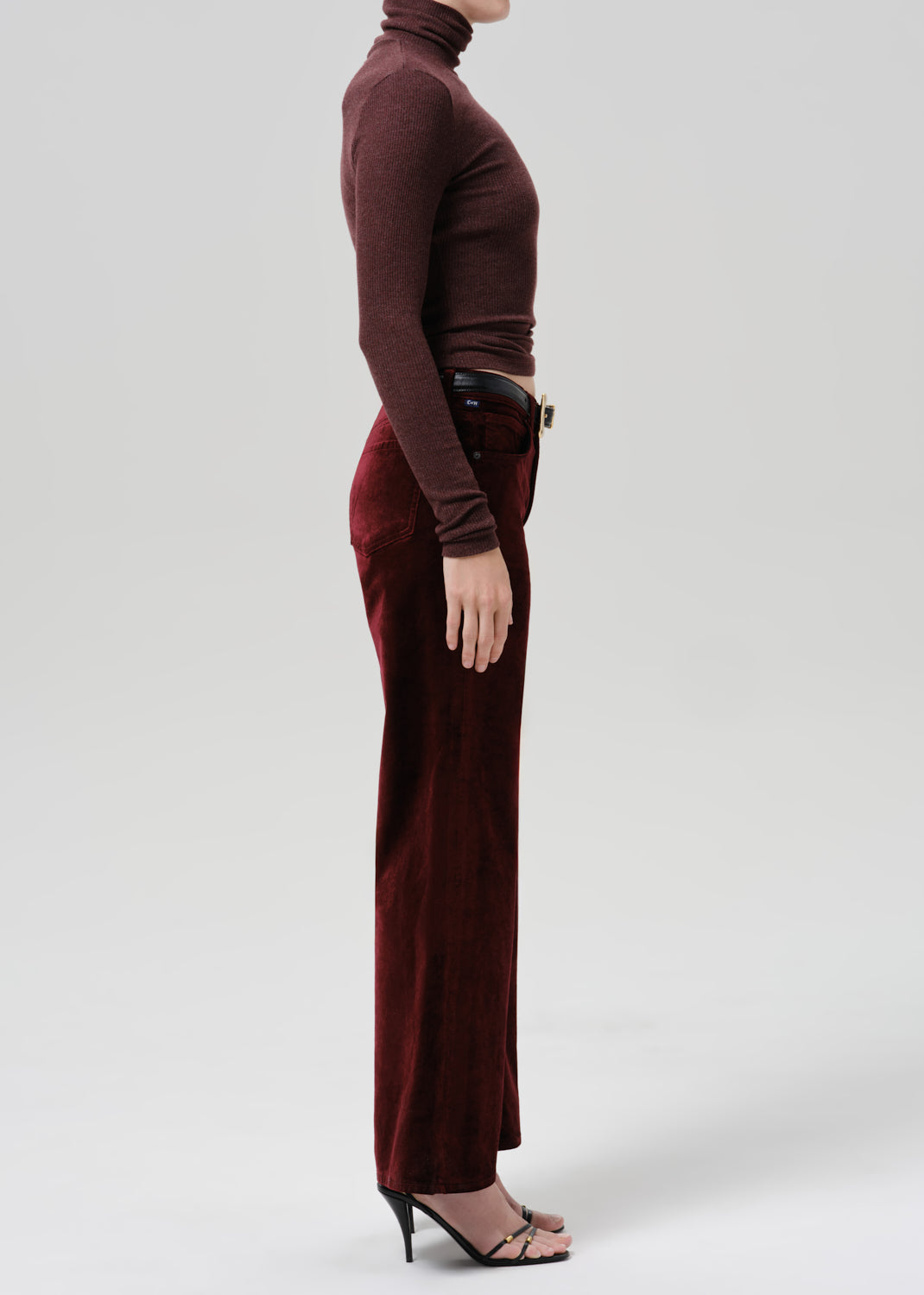 Person wearing a burgundy fitted turtleneck with burgundy wide leg pants viewed from the side on a grey background