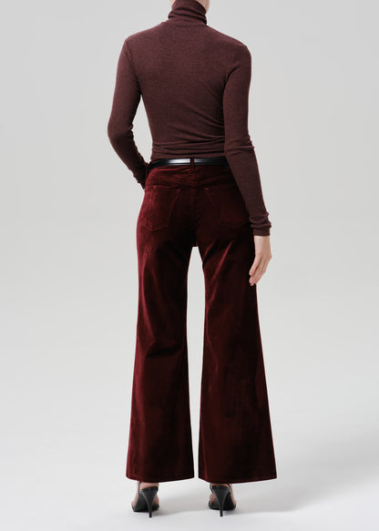 Person wearing a burgundy fitted turtleneck with burgundy wide leg pants viewed from the back on a grey background