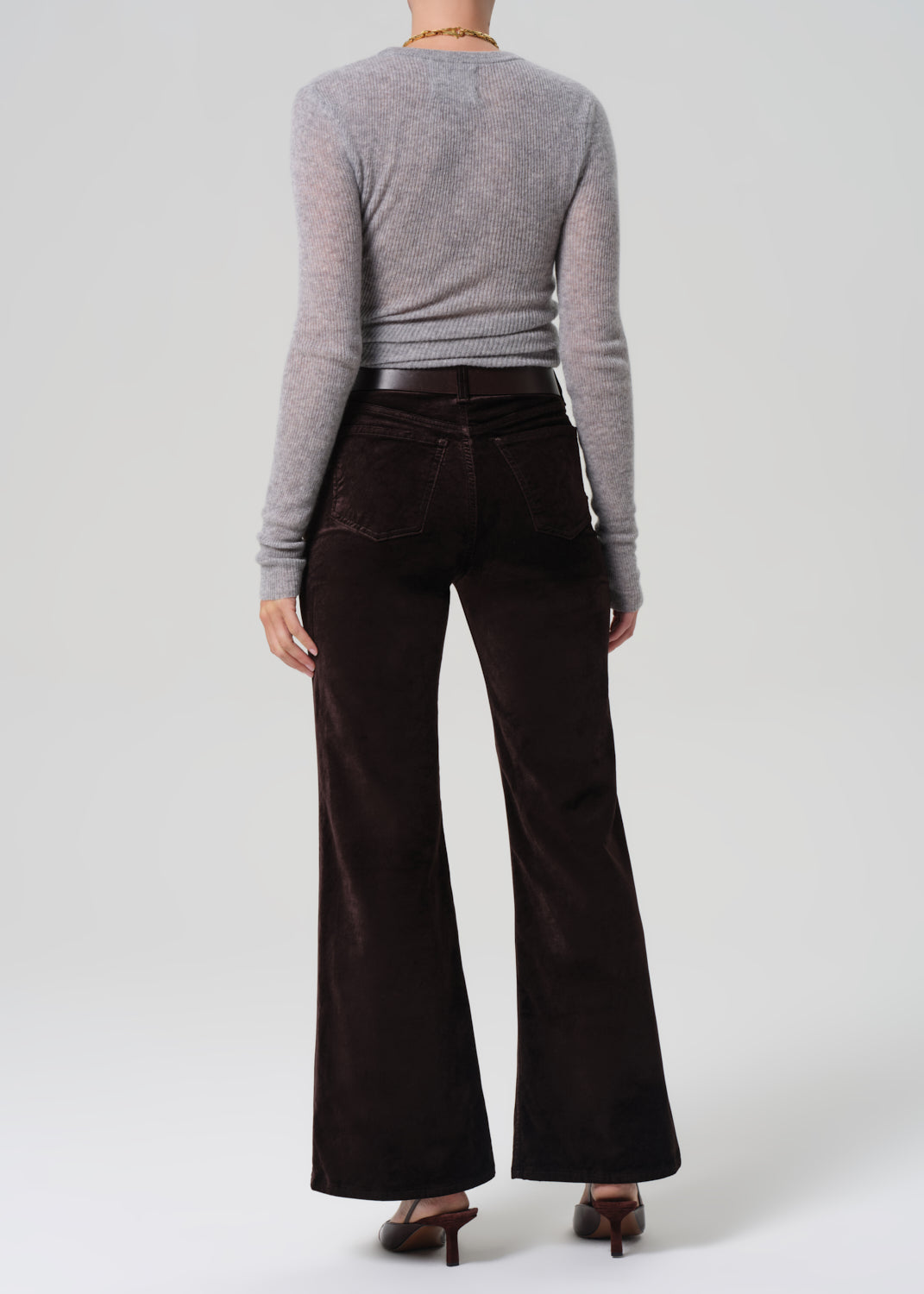 Person wearing a gray sweater and dark brown flared pants on a white background