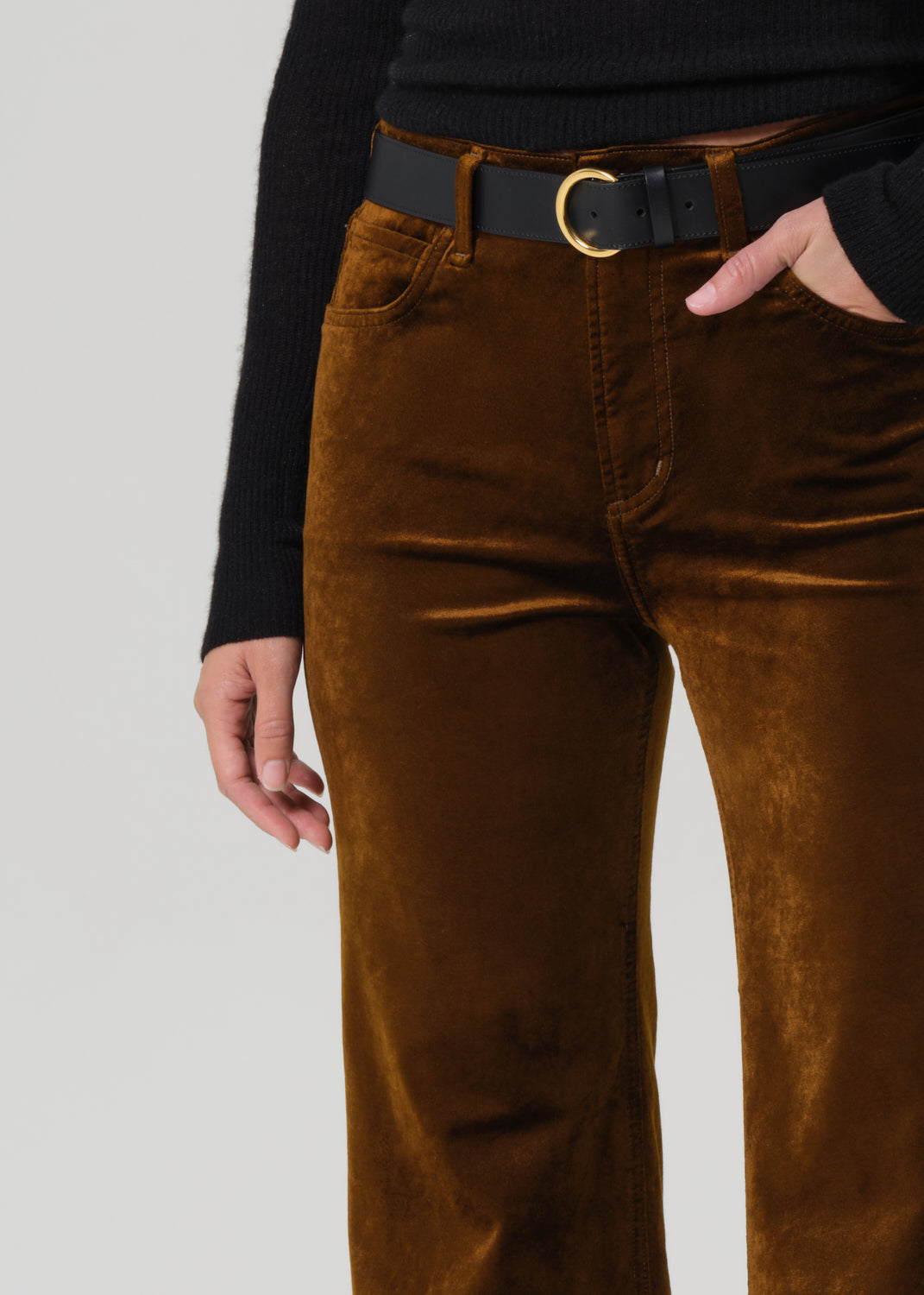 Brown velvet pants worn with a black belt on a light gray background