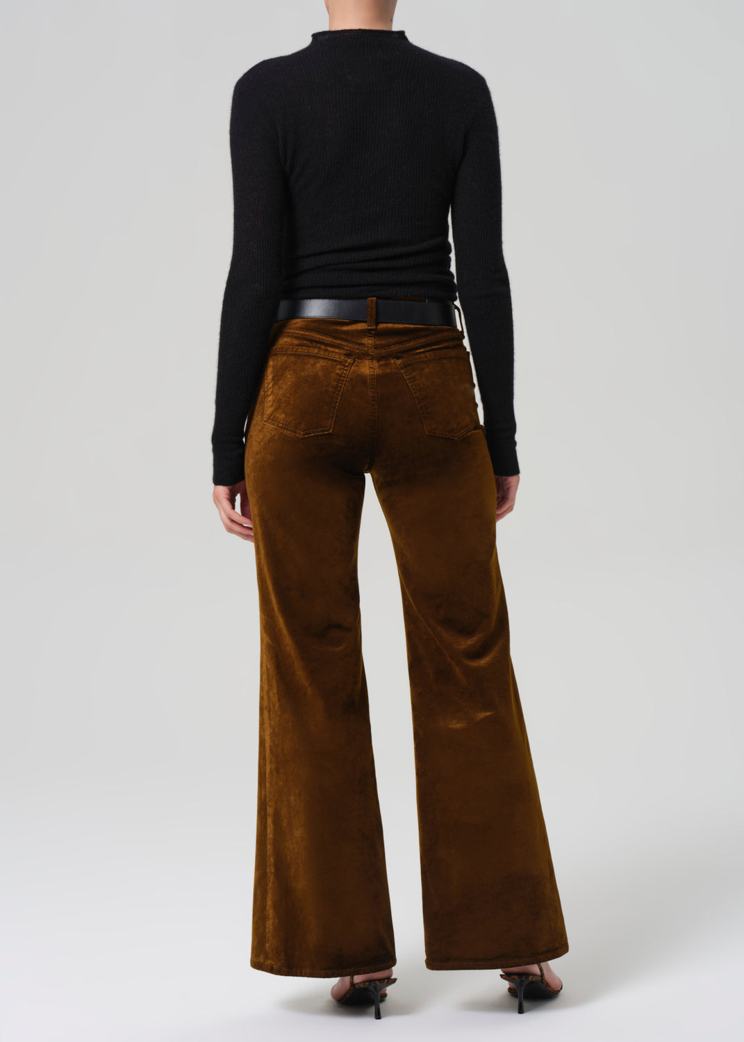 Person wearing brown velvet flared pants and a black long-sleeve top on a white background