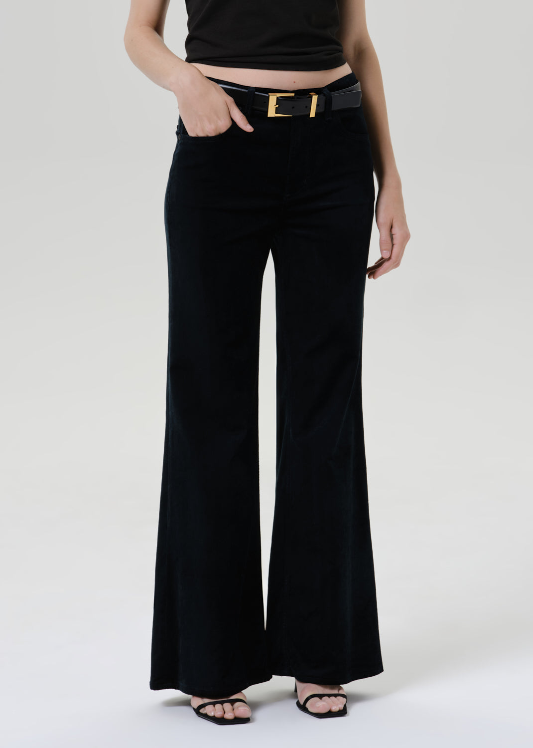 Person wearing a black fitted cap sleeve tee with black wide leg pants on a grey background