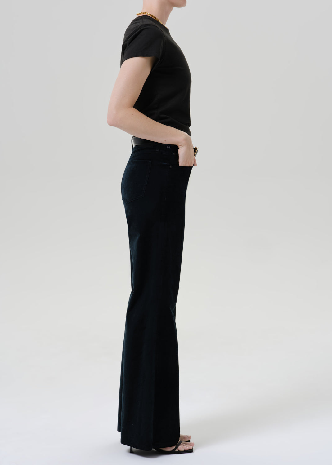 Person wearing a black fitted cap sleeve tee with black wide leg pants viewed from the side on a grey background