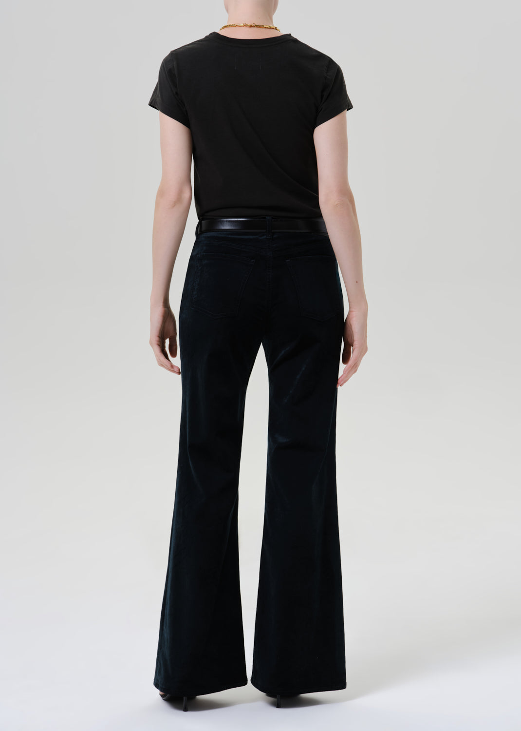 Person wearing a black fitted cap sleeve tee with black wide leg pants viewed from the back on a grey background