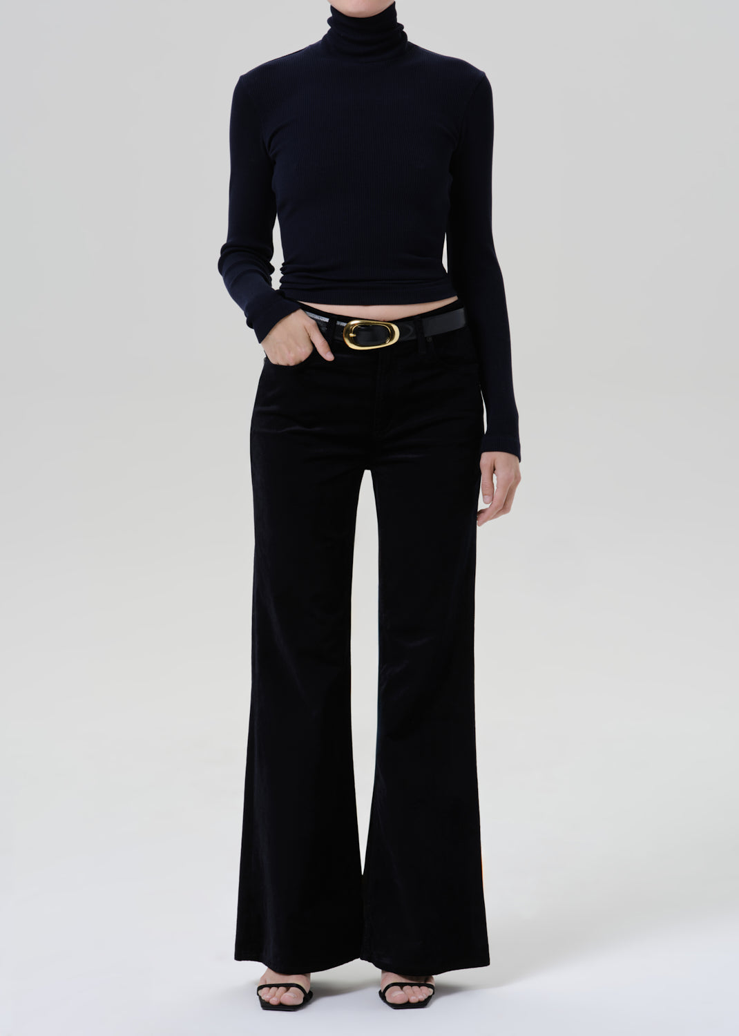 Person wearing a black fitted turtleneck with black wide leg trousers on a grey background