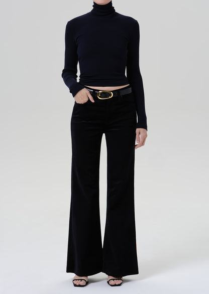 Person wearing a black fitted turtleneck with black wide leg trousers on a grey background