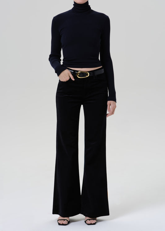 Person wearing a black fitted turtleneck with black wide leg trousers on a grey background
