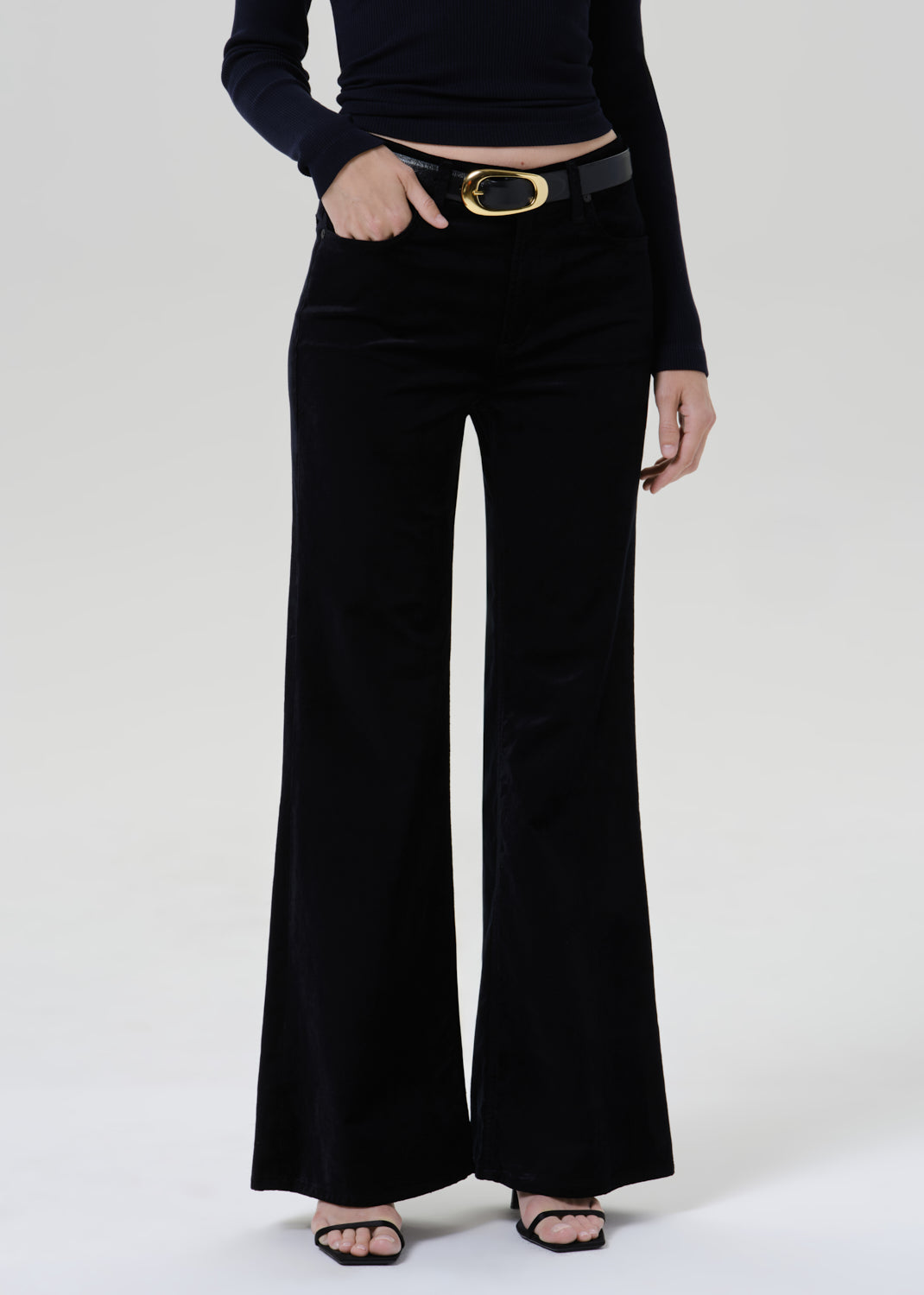 Person wearing a black fitted turtleneck with black wide leg trousers on a grey background
