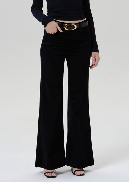 Person wearing a black fitted turtleneck with black wide leg trousers on a grey background