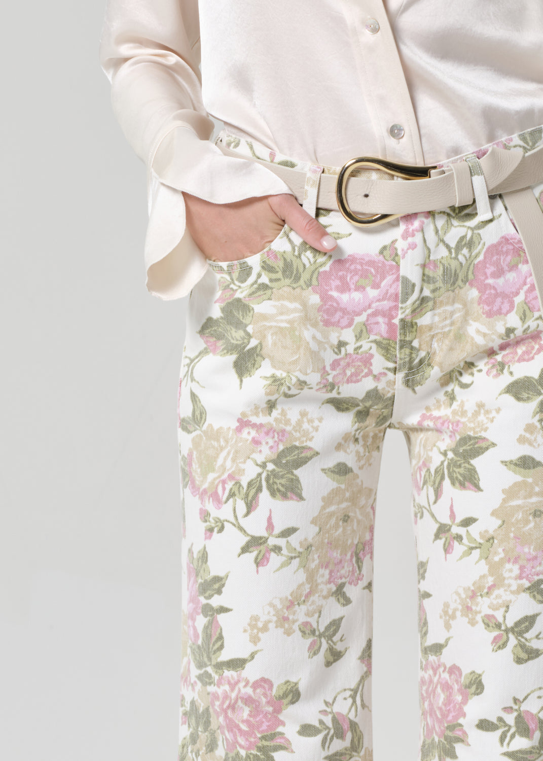 Person wearing a cream shirt and floral flare jeans on a grey background