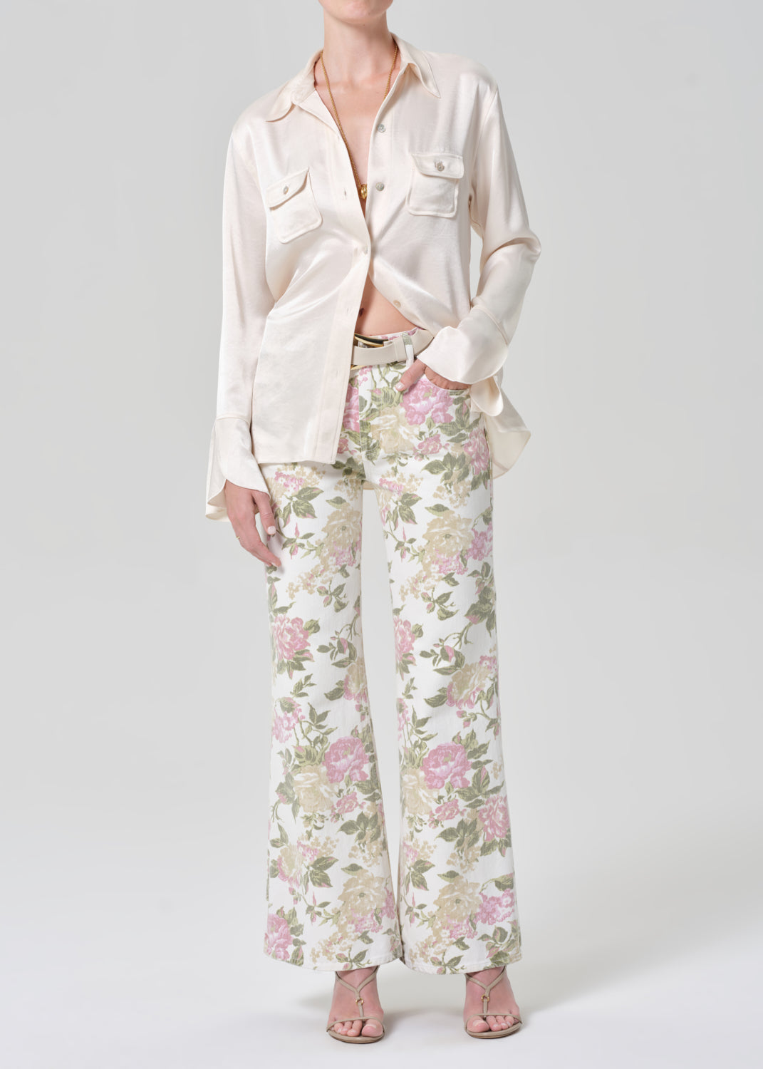 Person wearing a cream shirt and floral flare jeans on a grey background
