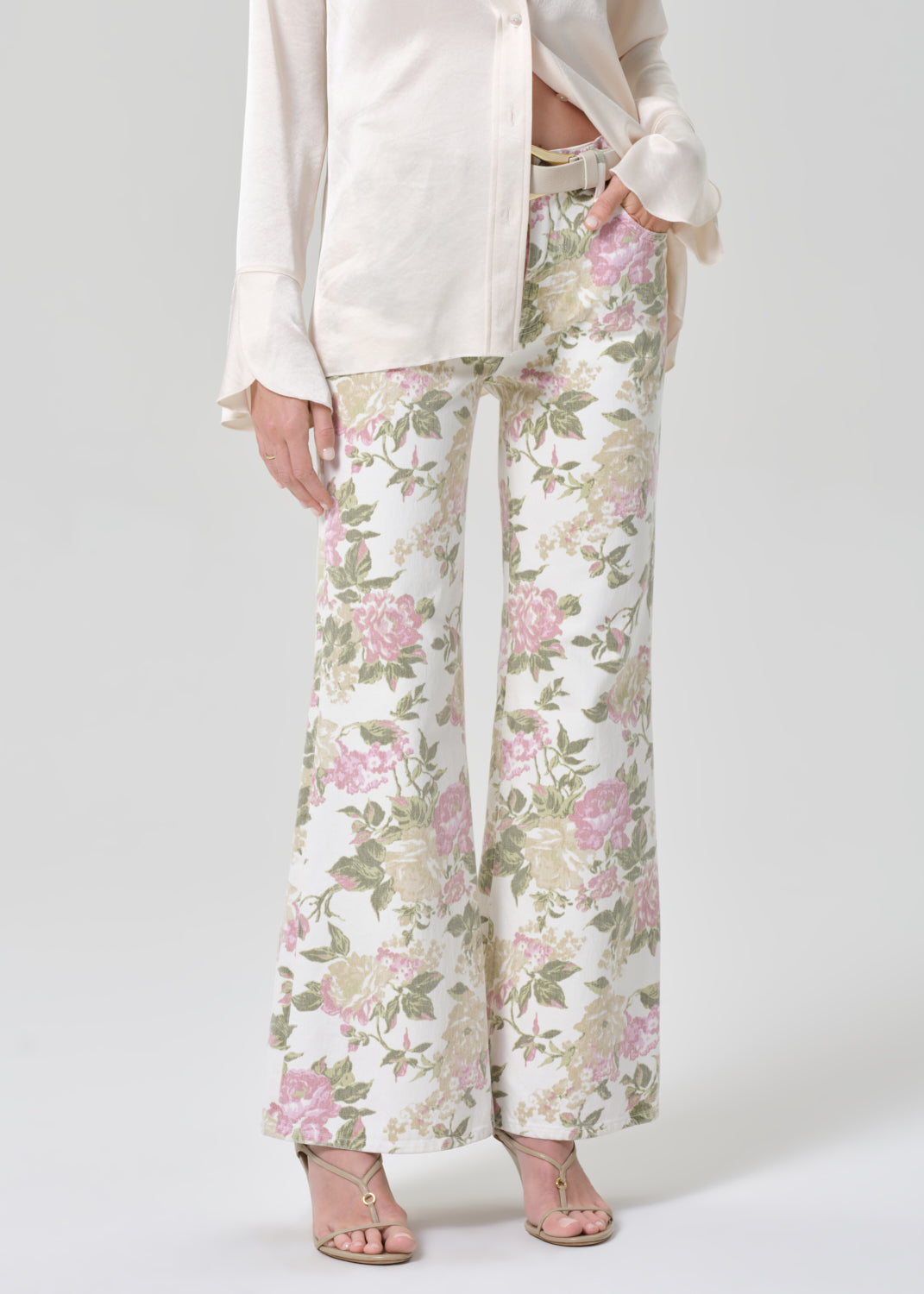 Person wearing a cream shirt and floral flare jeans on a grey background