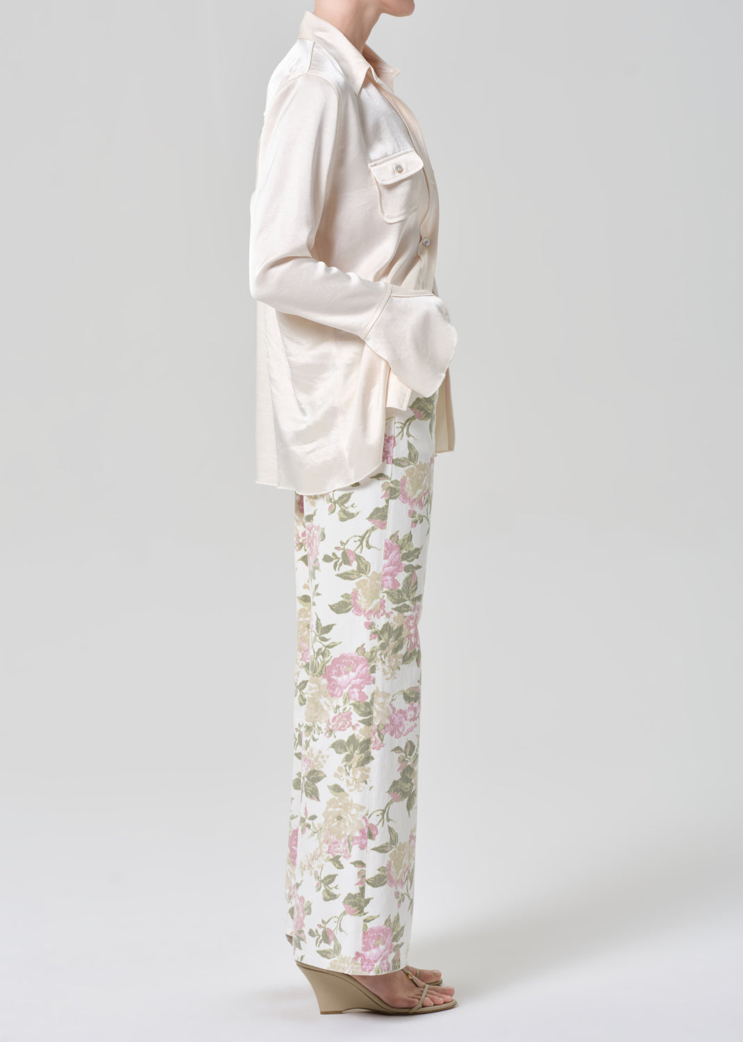 Person wearing a cream shirt and floral flare jeans on a grey background