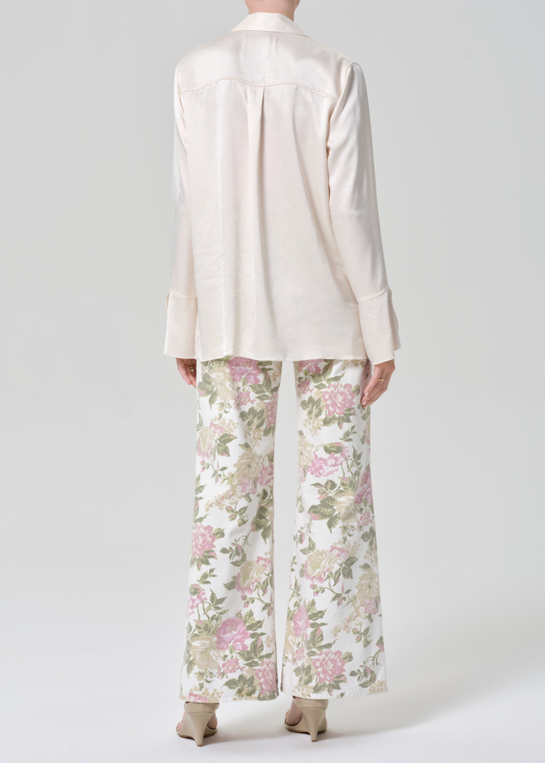 Person wearing a cream shirt and floral flare jeans on a grey background