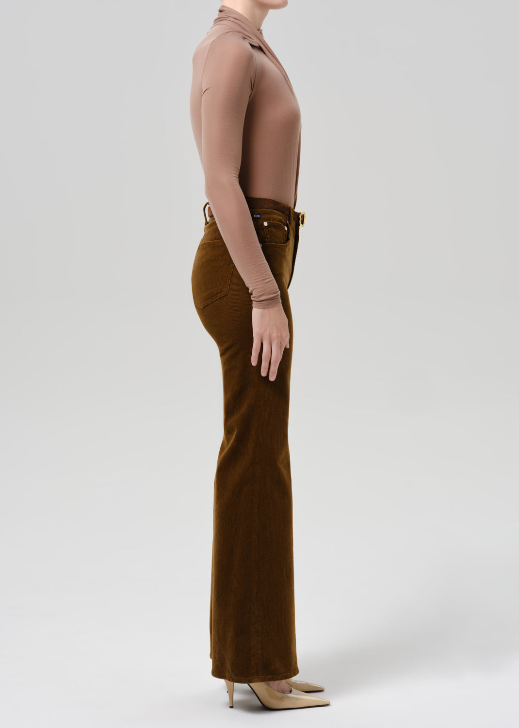 Person wearing tan bodysuit and orange flare corduroy pants on a grey background