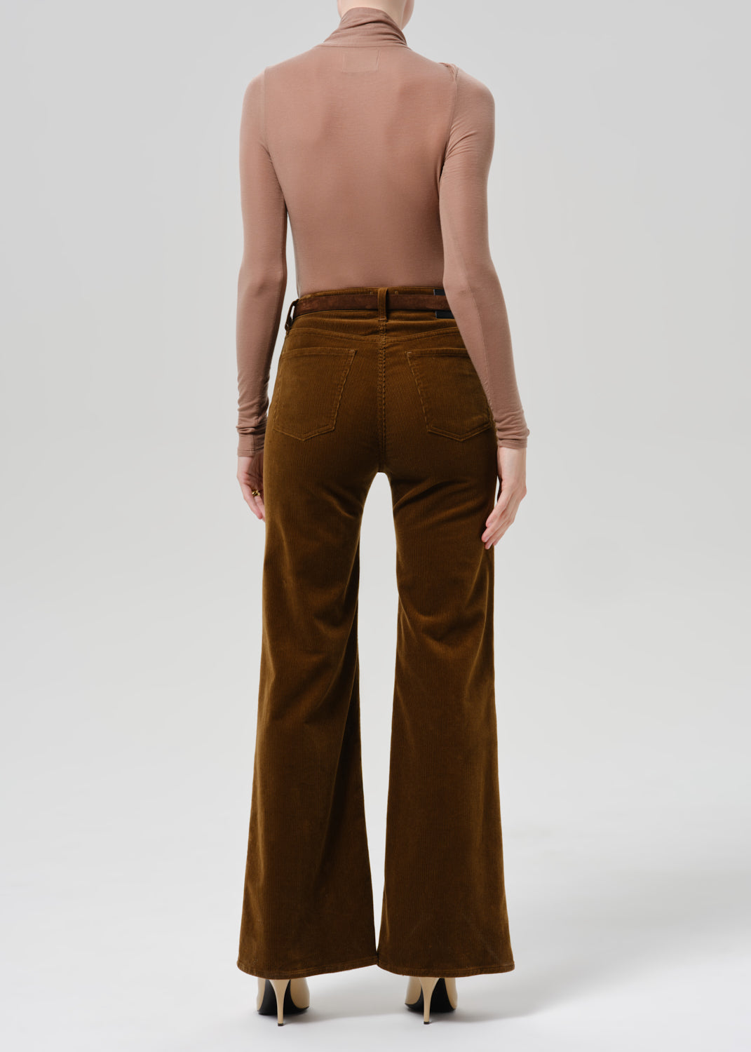 Person wearing tan bodysuit and orange flare corduroy pants on a grey background