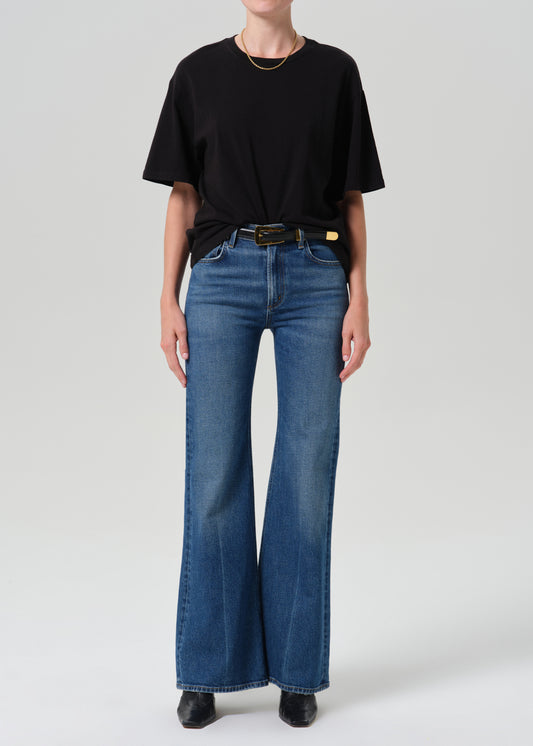 A model wearing a black short-sleeve t-shirt and blue high-waisted flare jeans with a black belt, standing against a grey background.