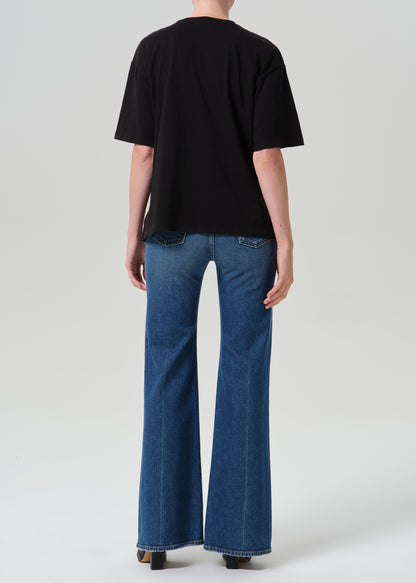 A model shown from the back wearing a black short-sleeve t-shirt and blue wide-leg flare jeans against a grey background.