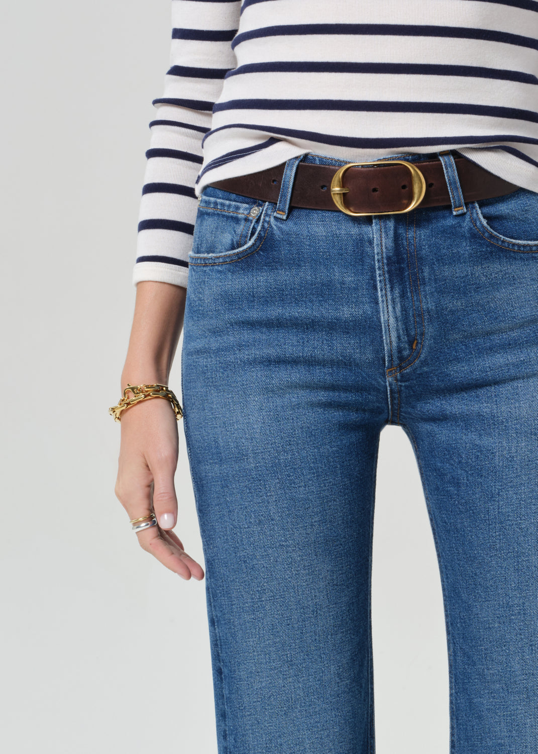 Person wearing a striped shirt and blue jeans on a grey background