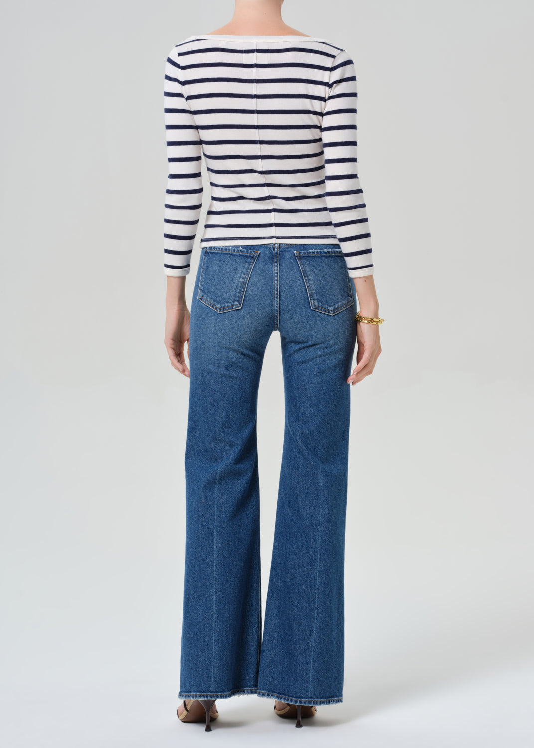 Person wearing a striped shirt and blue jeans on a grey background