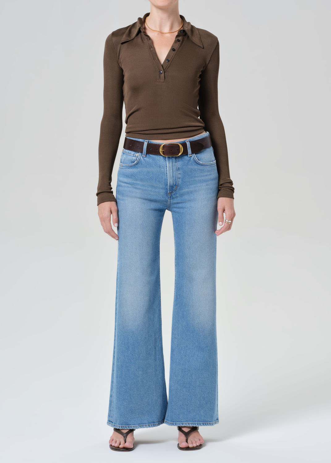 Person wearing a brown long-sleeve shirt and blue jeans on a grey background