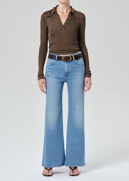 Person wearing a brown long-sleeve shirt and blue jeans on a grey background