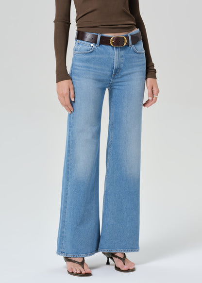 Person wearing blue jeans and a brown top on a grey background