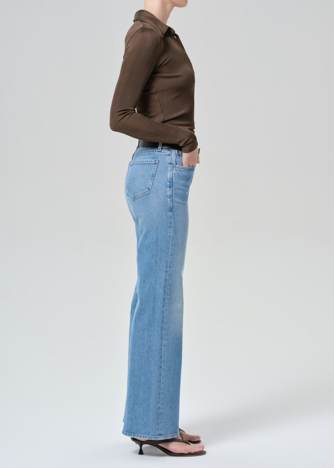 Person wearing a brown shirt and light blue jeans on a grey background