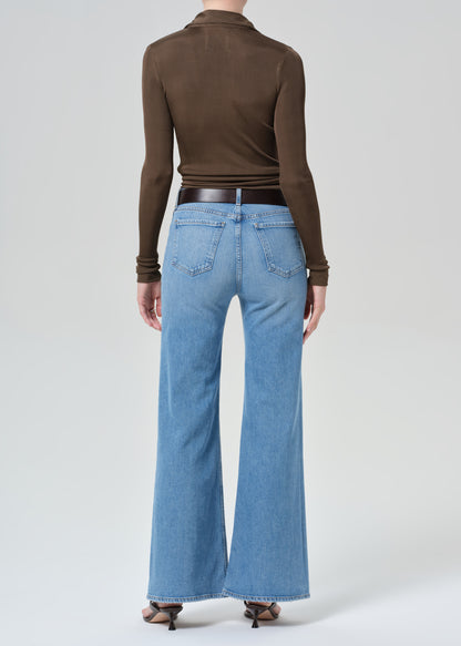 Person wearing a brown long-sleeve top and blue jeans on a grey background