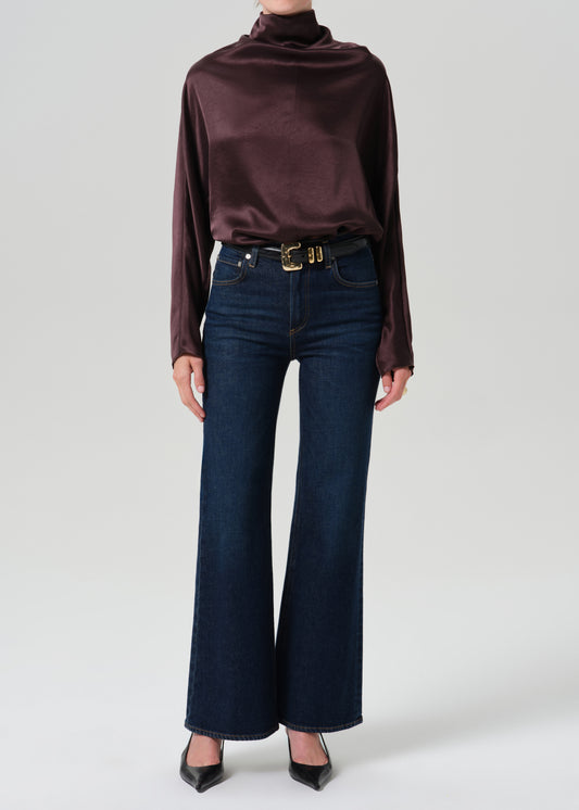 Person wearing a dark brown long sleeve draped blouse on a grey background