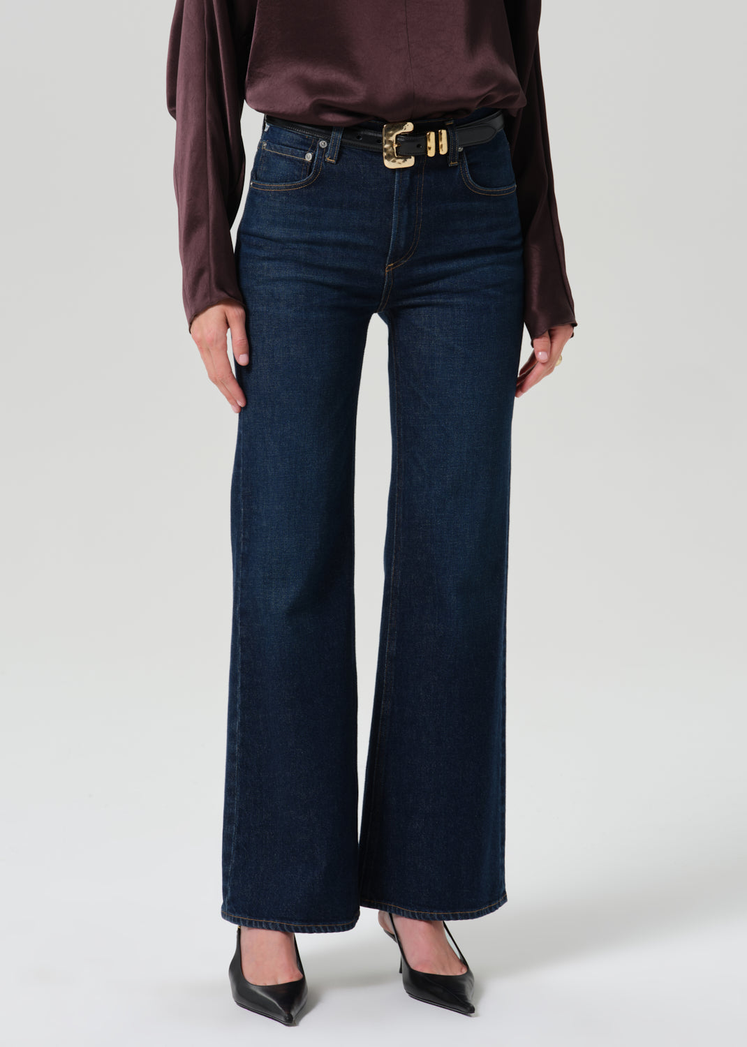 Person wearing a dark brown long sleeve draped blouse with dark indigo cropped wide leg jeans on a grey background