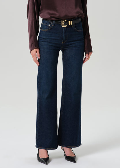 Person wearing a dark brown long sleeve draped blouse with dark indigo cropped wide leg jeans on a grey background