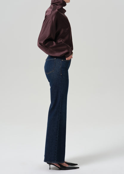 Person wearing a dark brown long sleeve draped blouse with dark indigo cropped wide leg jeans viewed from the side on a grey background