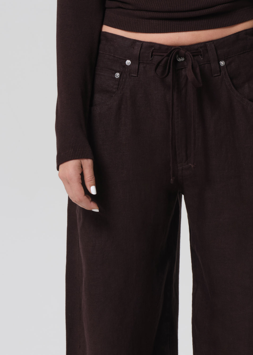 Person wearing a brown long-sleeve top and wide-leg pants on a grey background