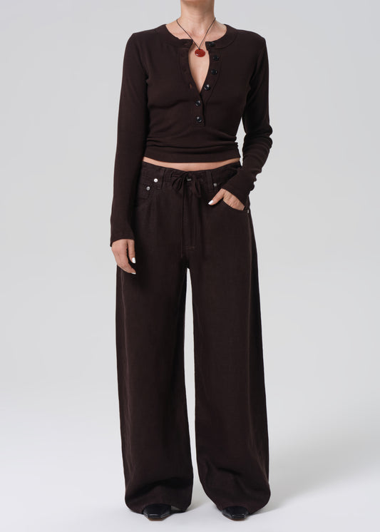 Person wearing a brown long-sleeve top and wide-leg pants on a grey background