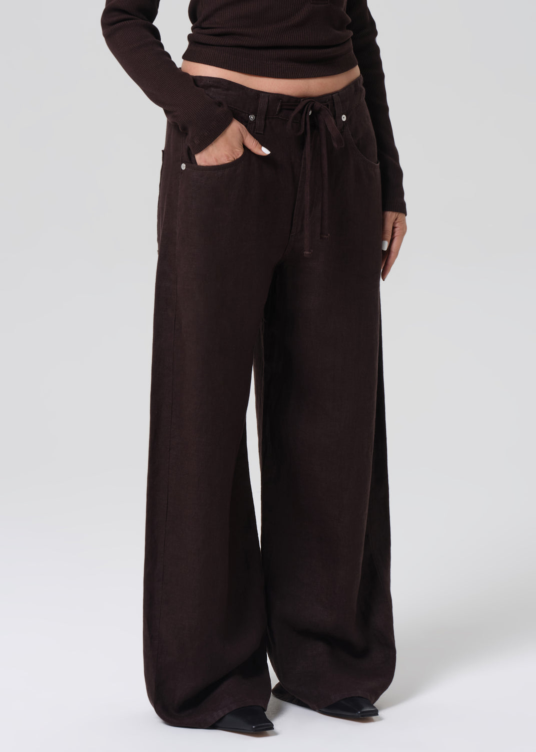 Person wearing a brown long-sleeve top and wide-leg pants on a grey background