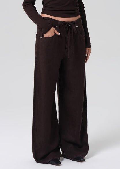 Person wearing a brown long-sleeve top and wide-leg pants on a grey background